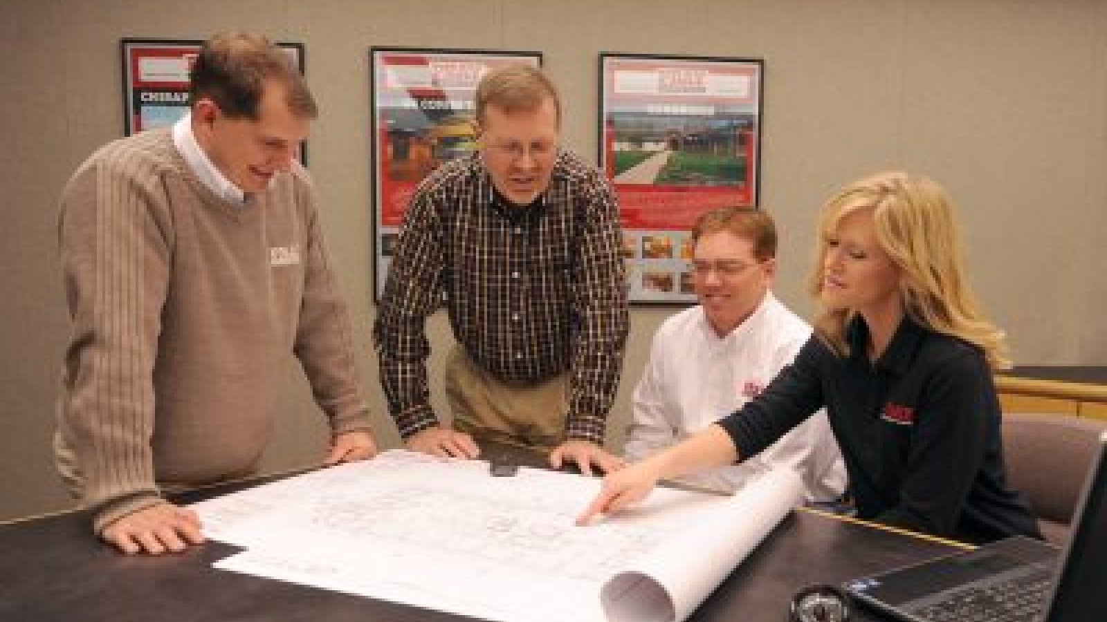 A conference room with four employees reviewing building plans.